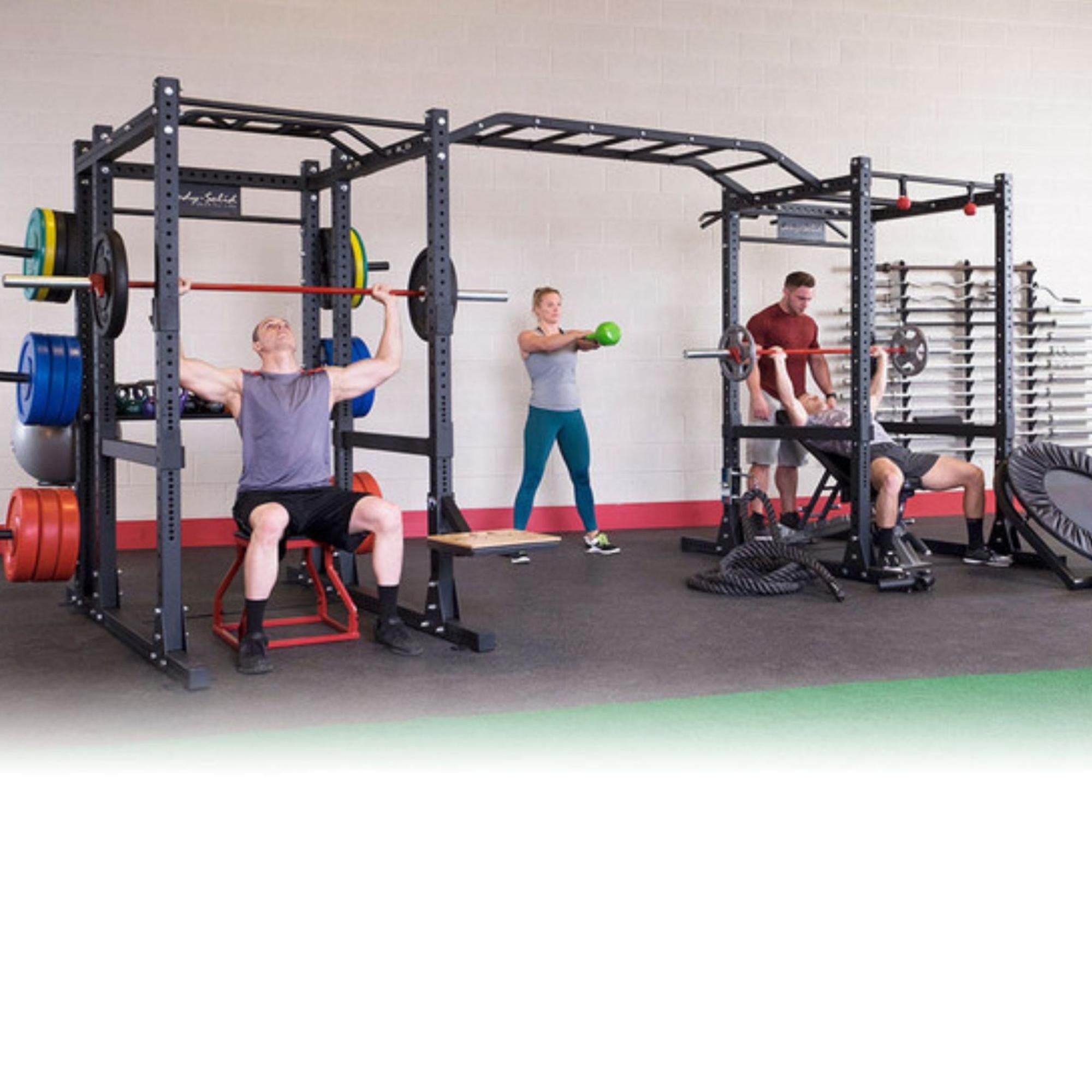 Body-Solid Pro ClubLine Double Power Racks with Rear Extensions and Monkey Bars with Safety Straps SPR1000SSDBBACK A group of four people exercising on a large, multi-station black fitness rig in a gym