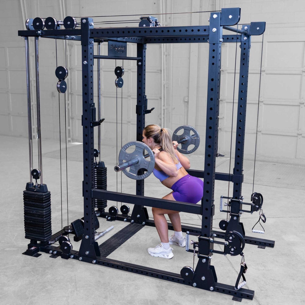 Body-Solid Pro ClubLine Functional Trainer Attachment SPRFTS Woman performing barbell squat inside Body-Solid Pro ClubLine SPRFTS functional trainer power rack, wearing purple workout outfit.