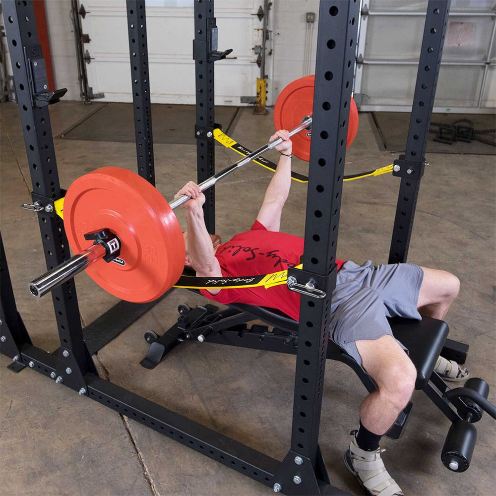 Body-Solid Pro ClubLine Power Rack with Safety Straps SPR1000SS Close-up of  strap safety system supporting loaded barbell with red and blue weight plates.
