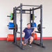 Body-Solid Pro ClubLine SPRBACK Power Rack Rear Extension SPRBACK Man performing a barbell squat inside a Body-Solid power rack loaded with colorful weight plates in a gym setting.