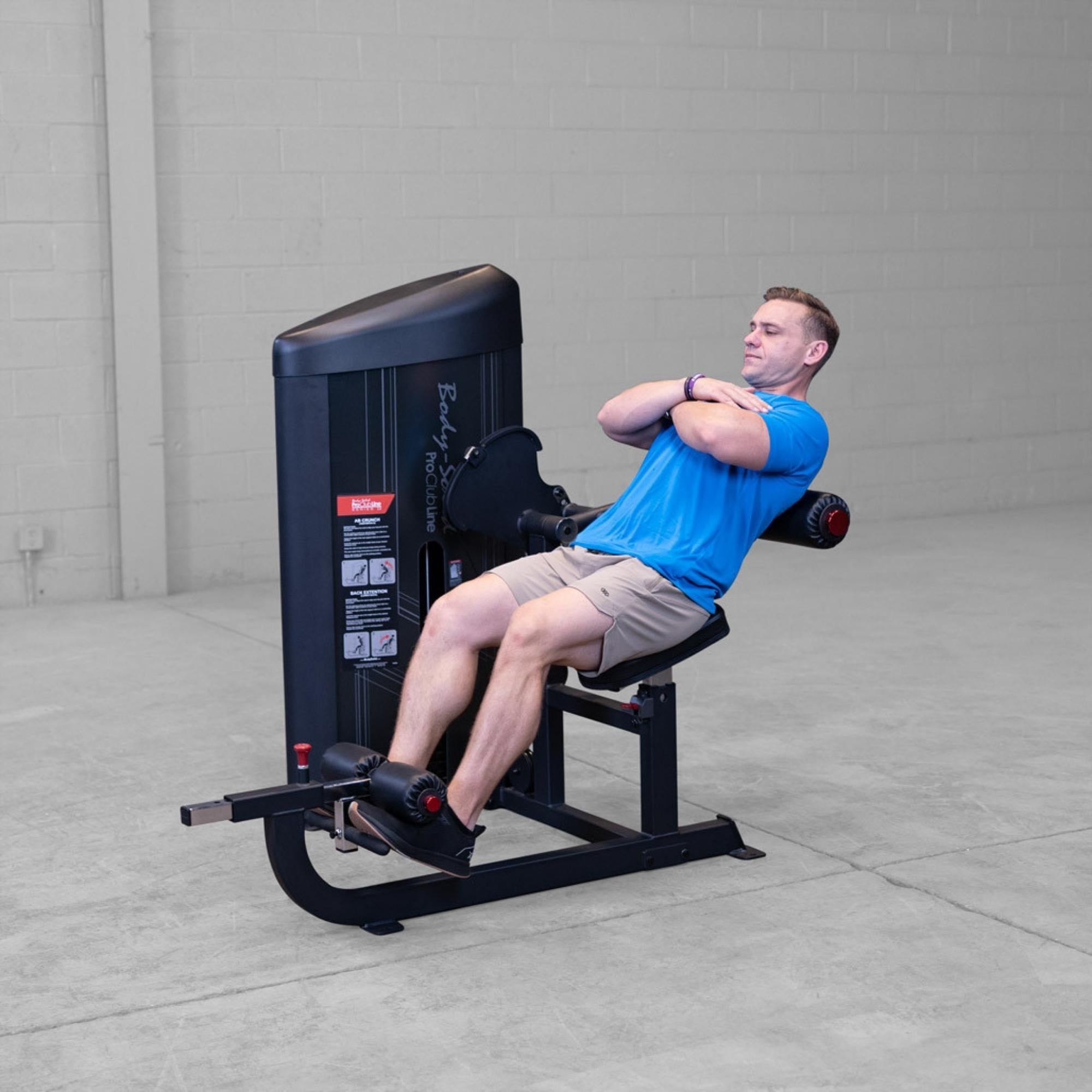 Body-Solid Pro ClubLine Series 2 Ab and Back S2ABBX Man doing seated leg extension with arms crossed using Body-Solid ProClubLine machine in a gym.