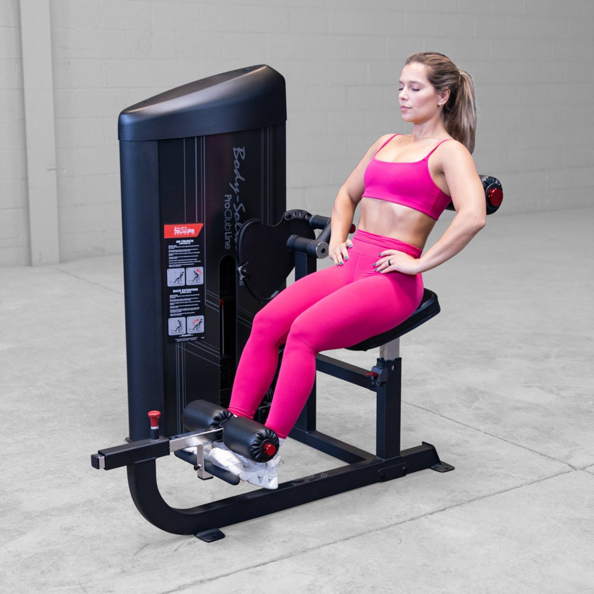 Body-Solid Pro ClubLine Series 2 Ab and Back S2ABBX Woman in pink gym outfit executing seated leg extension on Body-Solid ProClubLine strength machine.
