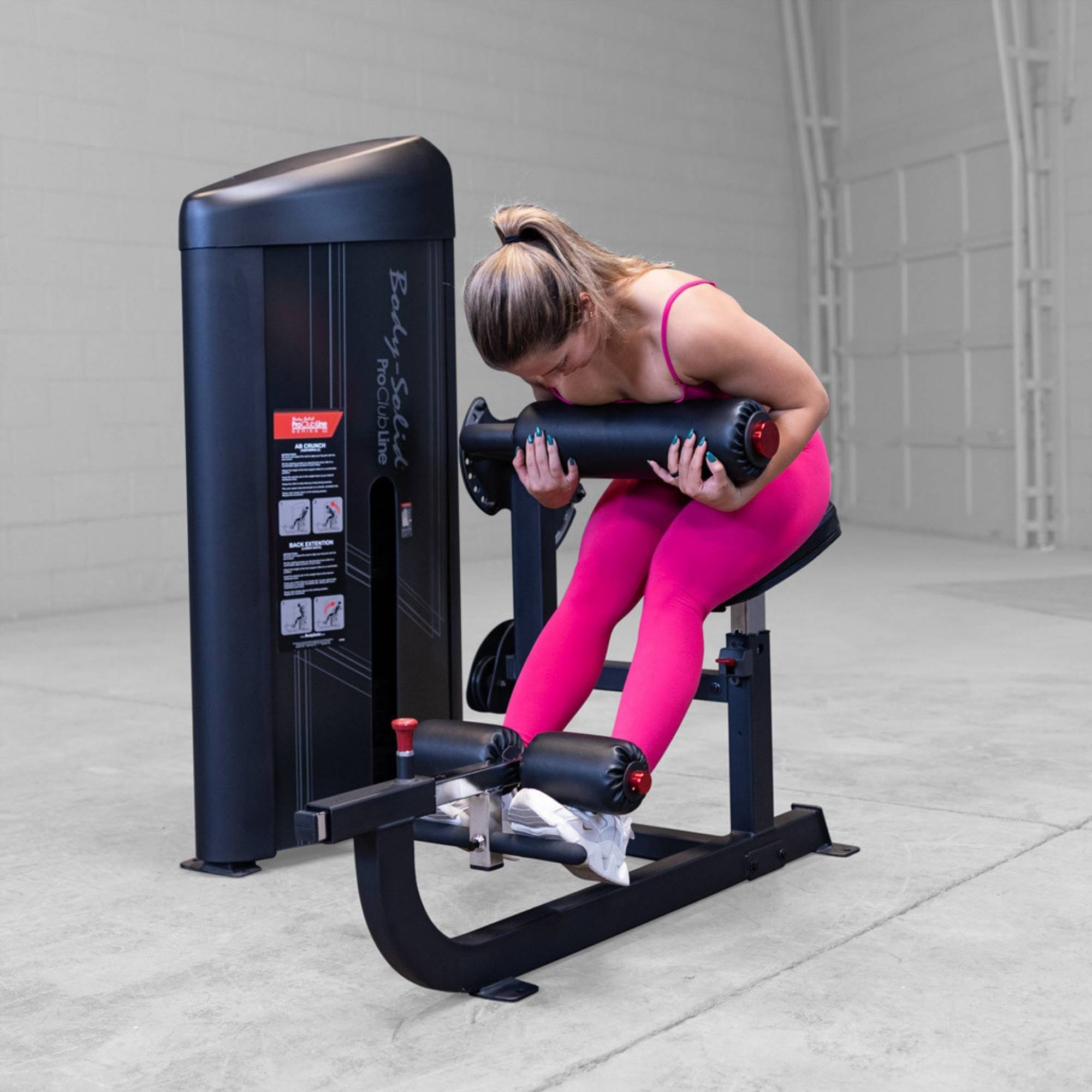 Body-Solid Pro ClubLine Series 2 Ab and Back S2ABBX Woman performing seated hamstring curl on a Body-Solid ProClubLine leg curl machine while wearing bright pink athletic attire.
