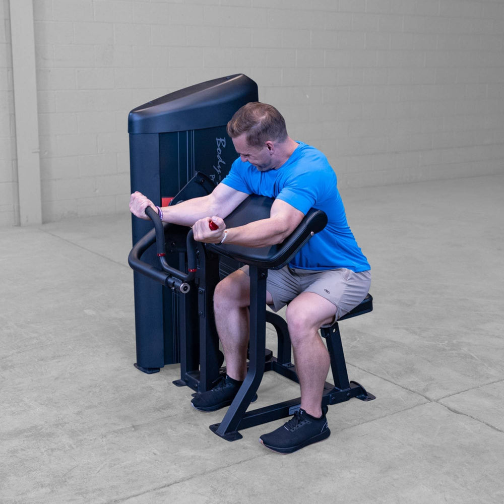 Body-Solid Pro ClubLine Series 2 Arm Curl S2ACX Man using angled curl handles on Body-Solid ProClubLine preacher curl machine in a fitness facility.
