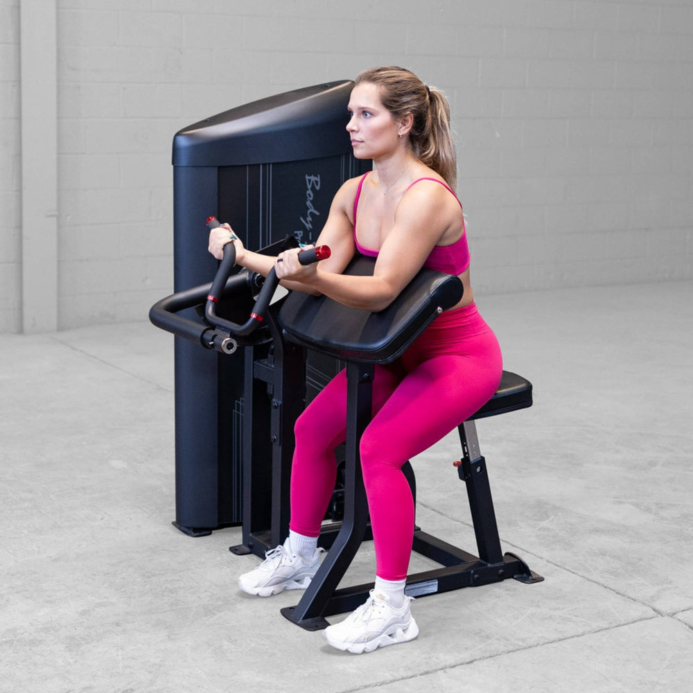 Body-Solid Pro ClubLine Series 2 Arm Curl S2ACX Woman seated and gripping angled curl handles while using a Body-Solid ProClubLine arm curl machine.
