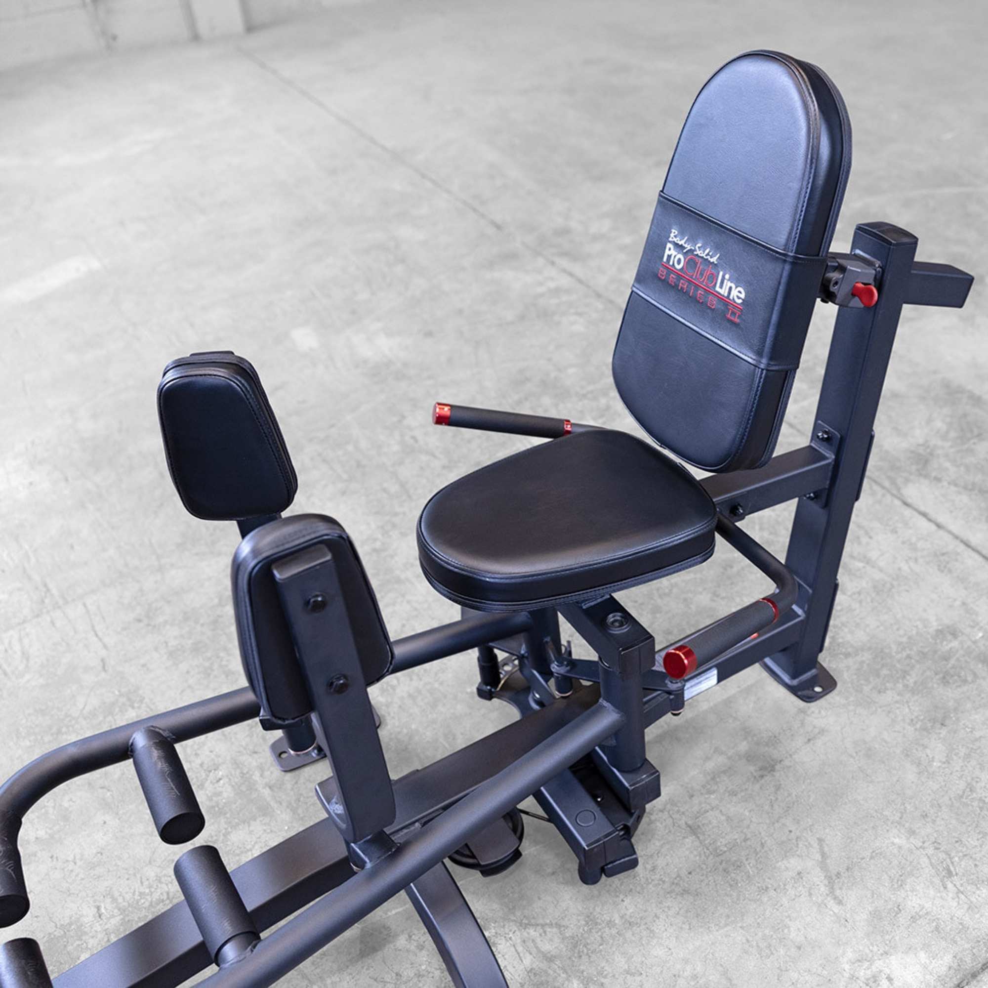 Body-Solid Pro ClubLine Series 2 Inner Outer Thigh S2IOTX Close-up view of the hip abductor machine seat, padded leg supports, and adjustment handles on a concrete gym floor