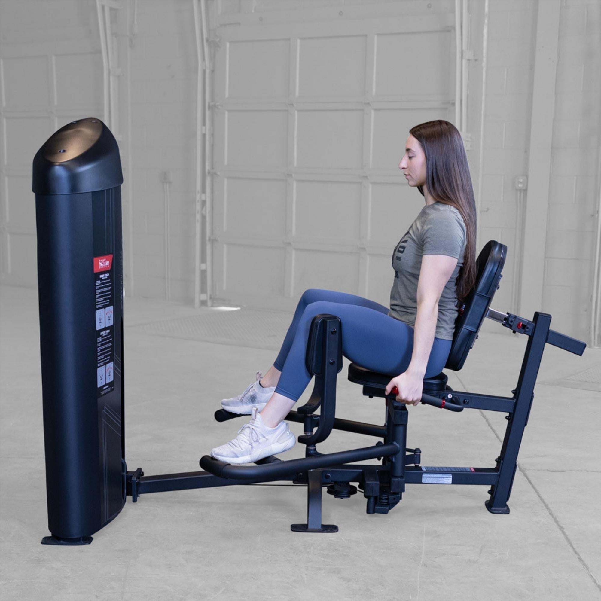 Body-Solid Pro ClubLine Series 2 Inner Outer Thigh S2IOTX Woman seated on a Body-Solid Pro Club Line hip abductor machine, holding handles and spreading legs outward during exercise.