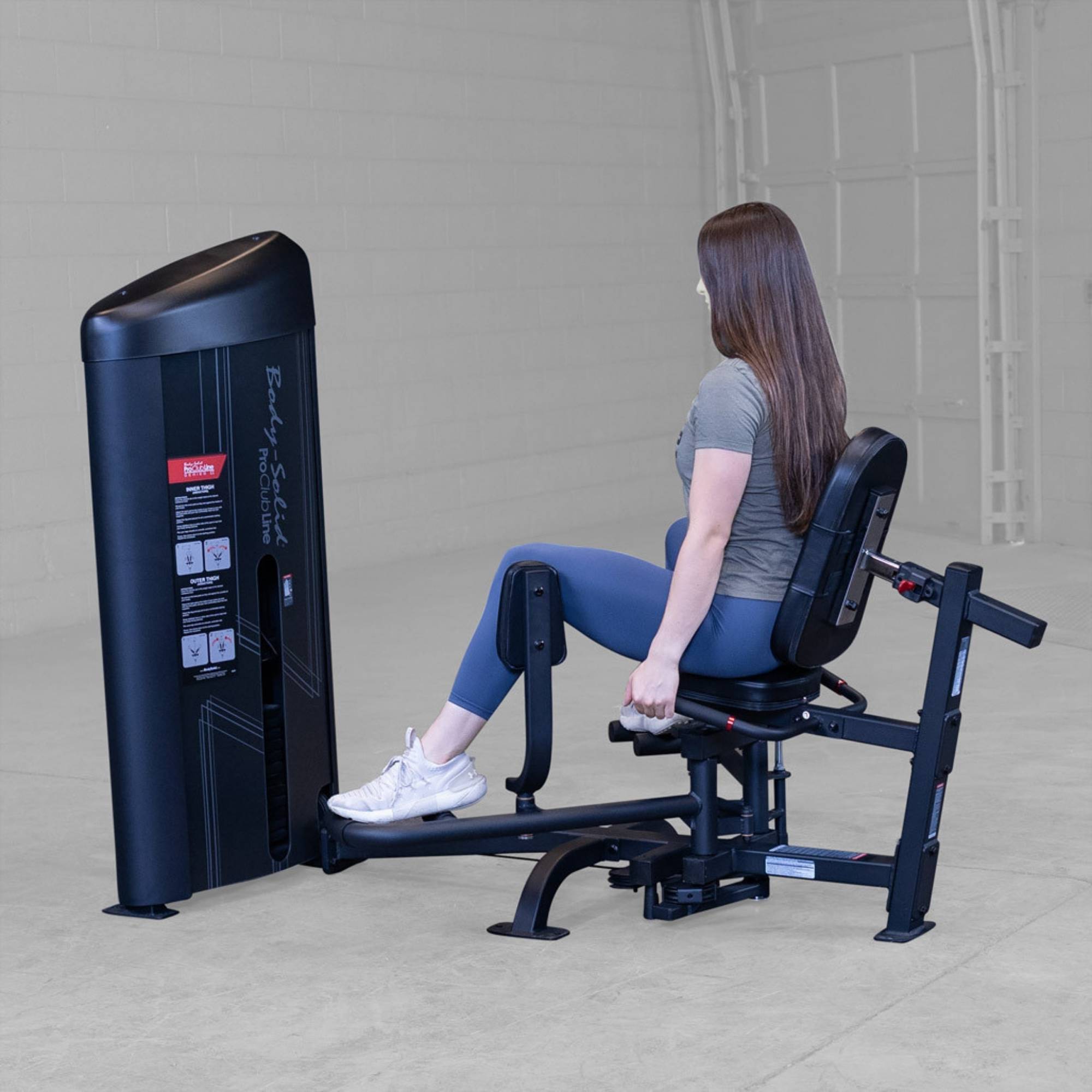 Body-Solid Pro ClubLine Series 2 Inner Outer Thigh S2IOTX Woman seated on hip abduction machine pushing leg pads outward while gripping side handles for stability