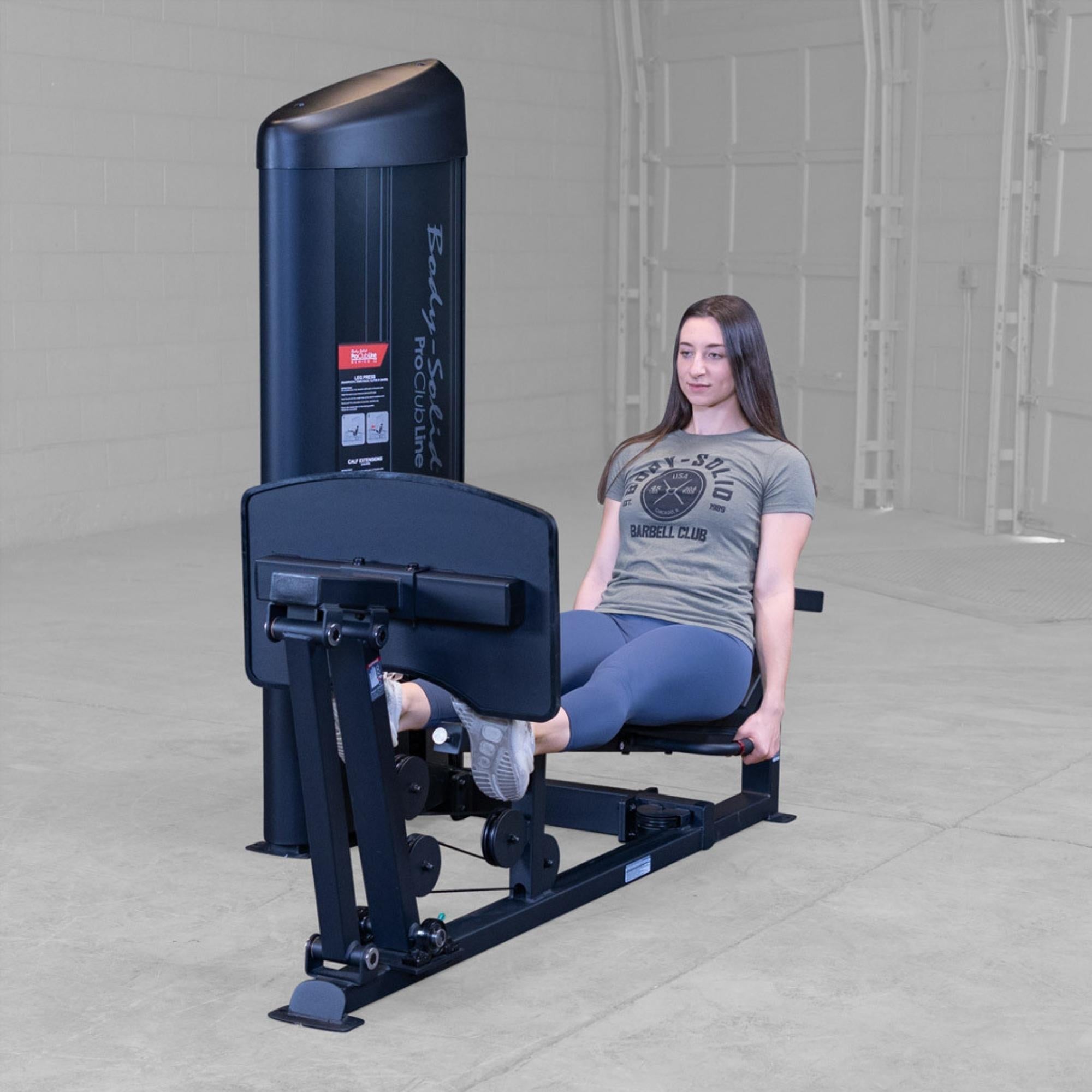 Body-Solid Pro ClubLine Series 2 Leg Calf Press S2LPCX Woman demonstrating seated leg press exercise on a Body-Solid ProClubLine machine, legs extended and back supported
