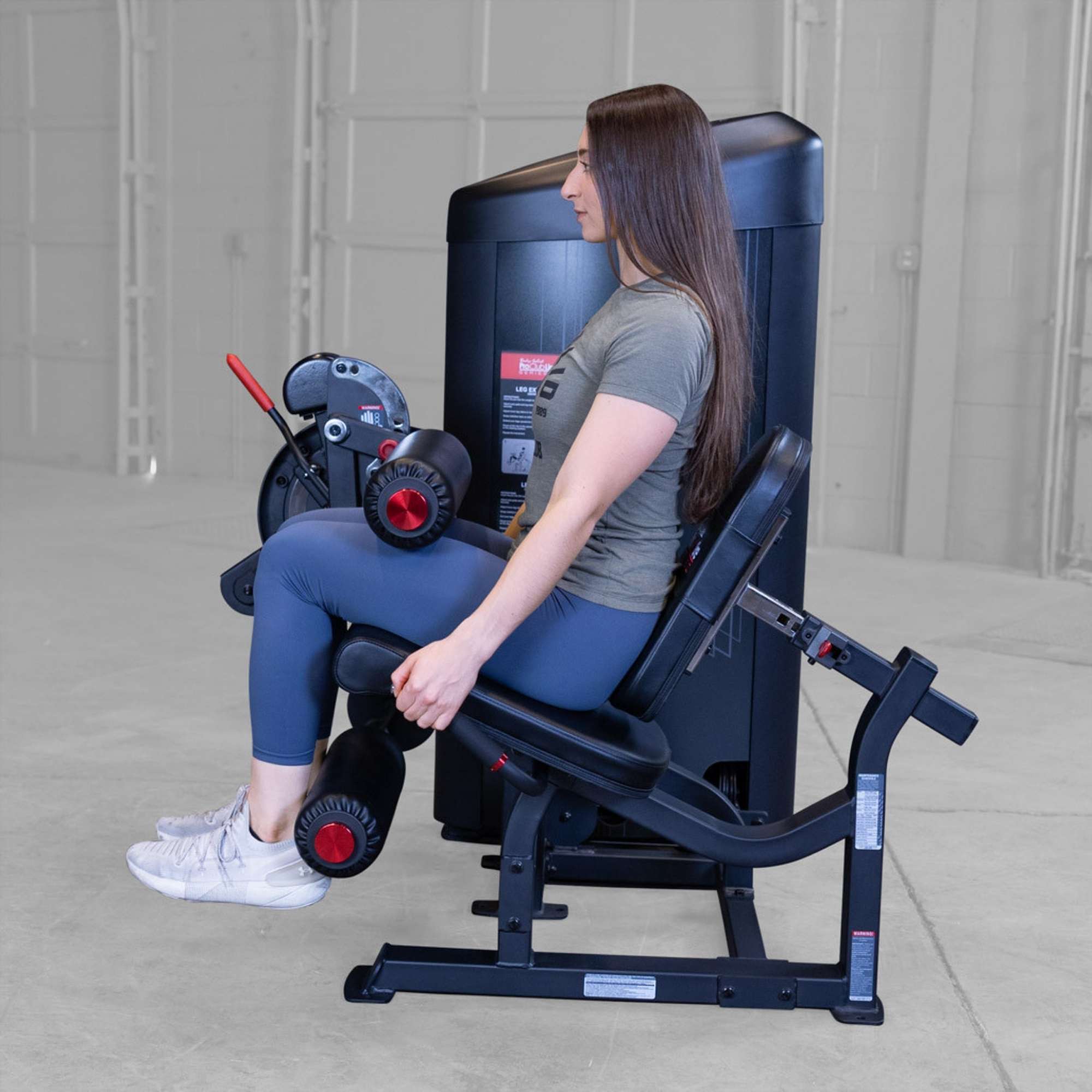 Body-Solid Pro Clubine Series 2 Leg Curl and Extension S2LECX Gym equipment demonstration showing woman seated with legs bent on a leg extension machine before lifting weight 