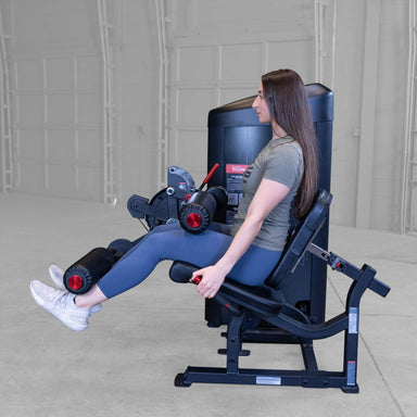 Body-Solid Pro Clubine Series 2 Leg Curl and Extension Leg extension S2LECX exercise in progress with woman raising legs outward against padded rollers on a strength training machine 