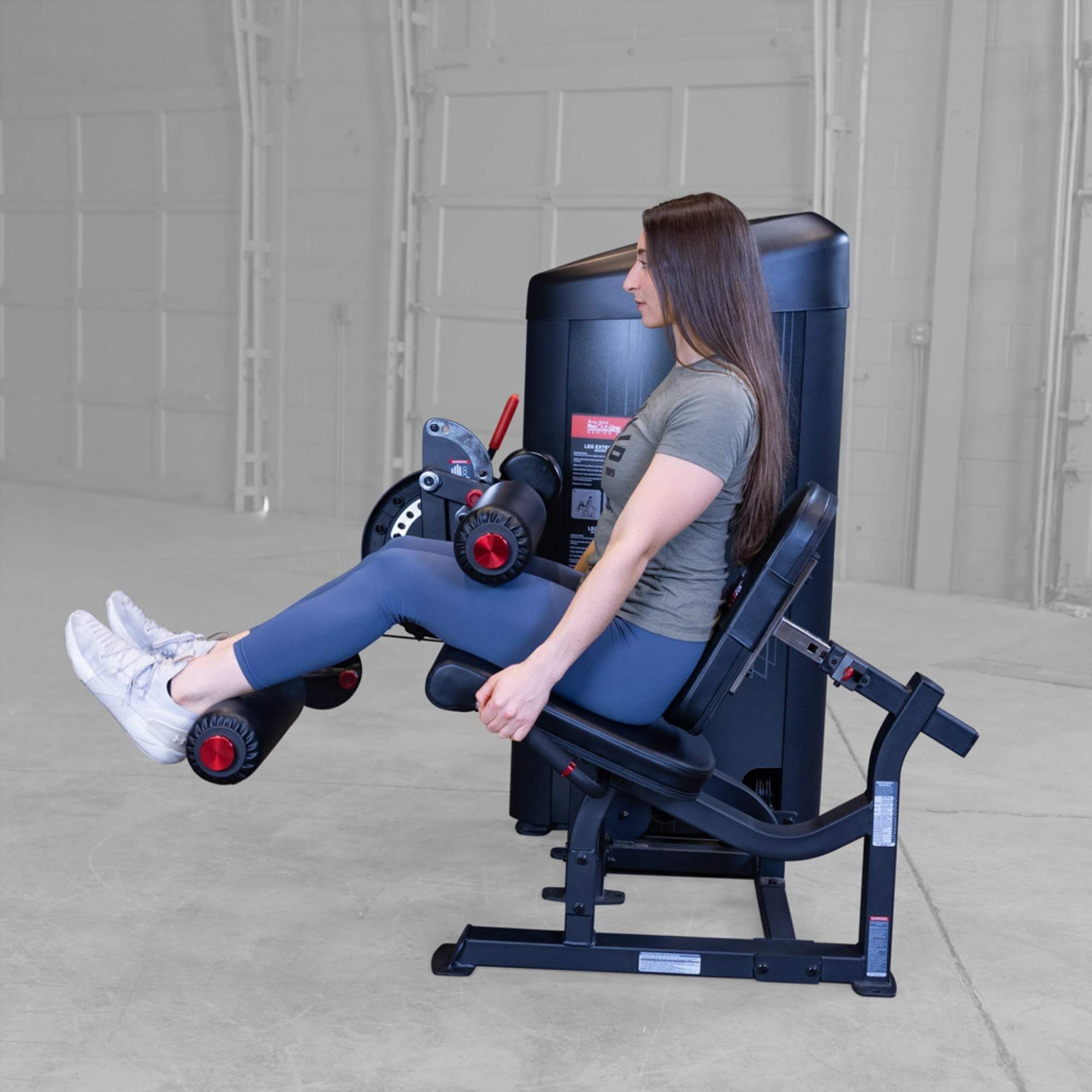 Body-Solid Pro Clubine Series 2 Leg Curl and Extension S2LECX Woman performing seated leg extension exercise on a Body-Solid ProClubLine machine in a gym setting, legs bent and starting position 