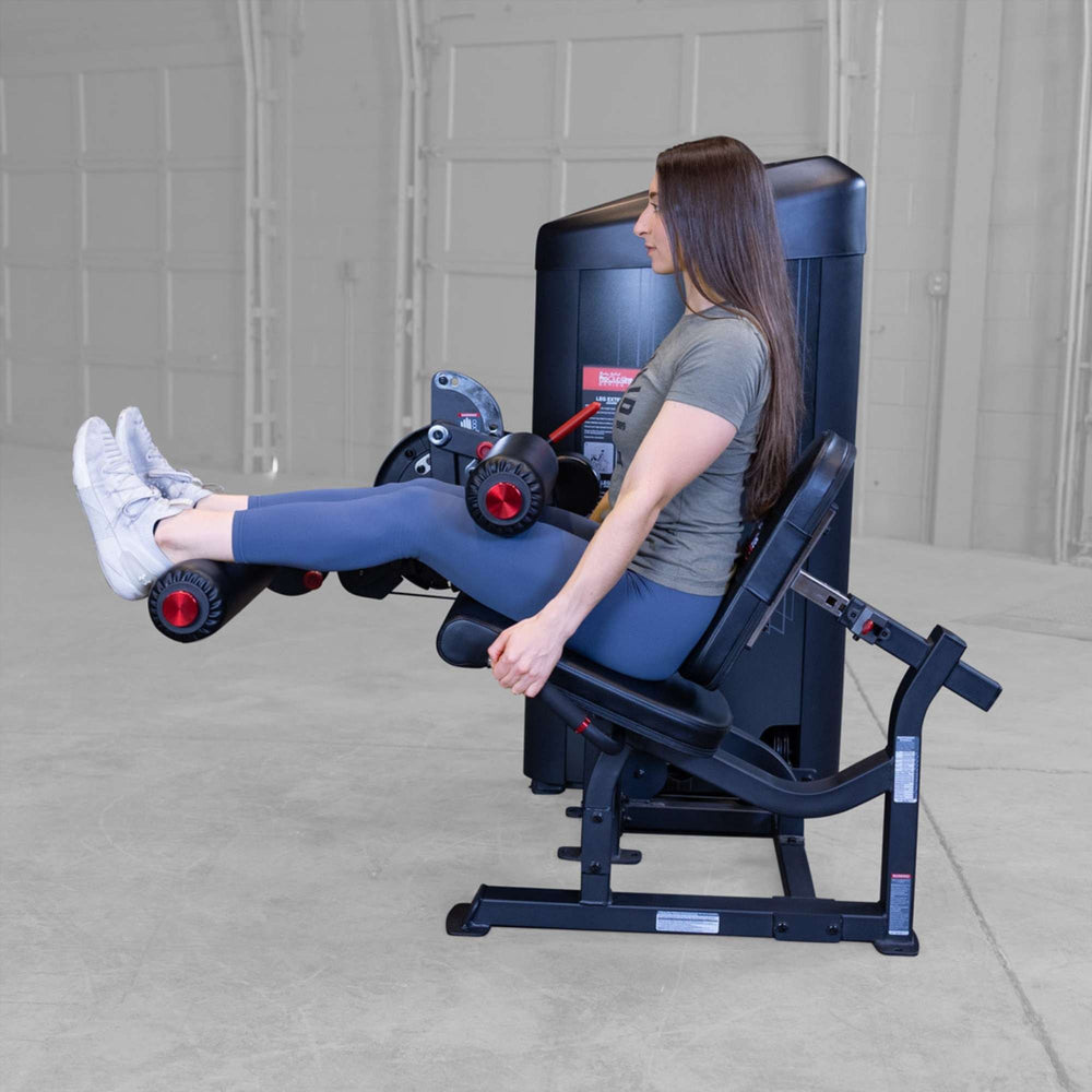 Body-Solid Pro Clubine Series 2 Leg Curl and Extension S2LECX Side view of woman lifting padded leg rollers on a leg extension machine, engaging quadriceps muscles during exercise 