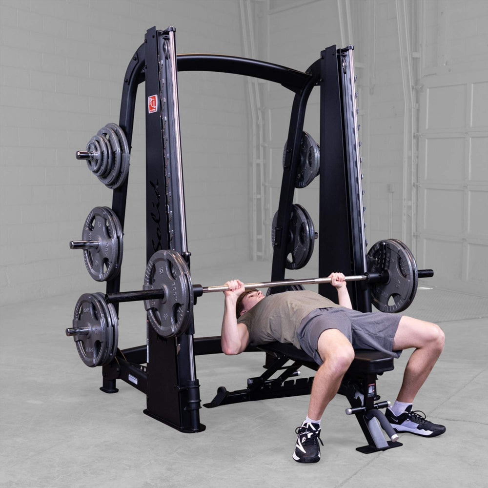 Body-Solid Proclub Counter Balanced Smith Machine SCB1000B A man performing a flat barbell bench press on a Smith machine in a gym setting.
