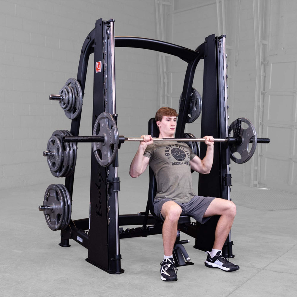 Body-Solid Proclub Counter Balanced Smith Machine SCB1000B A man performing a seated barbell shoulder press using a Smith machine with an adjustable bench in a gym.

