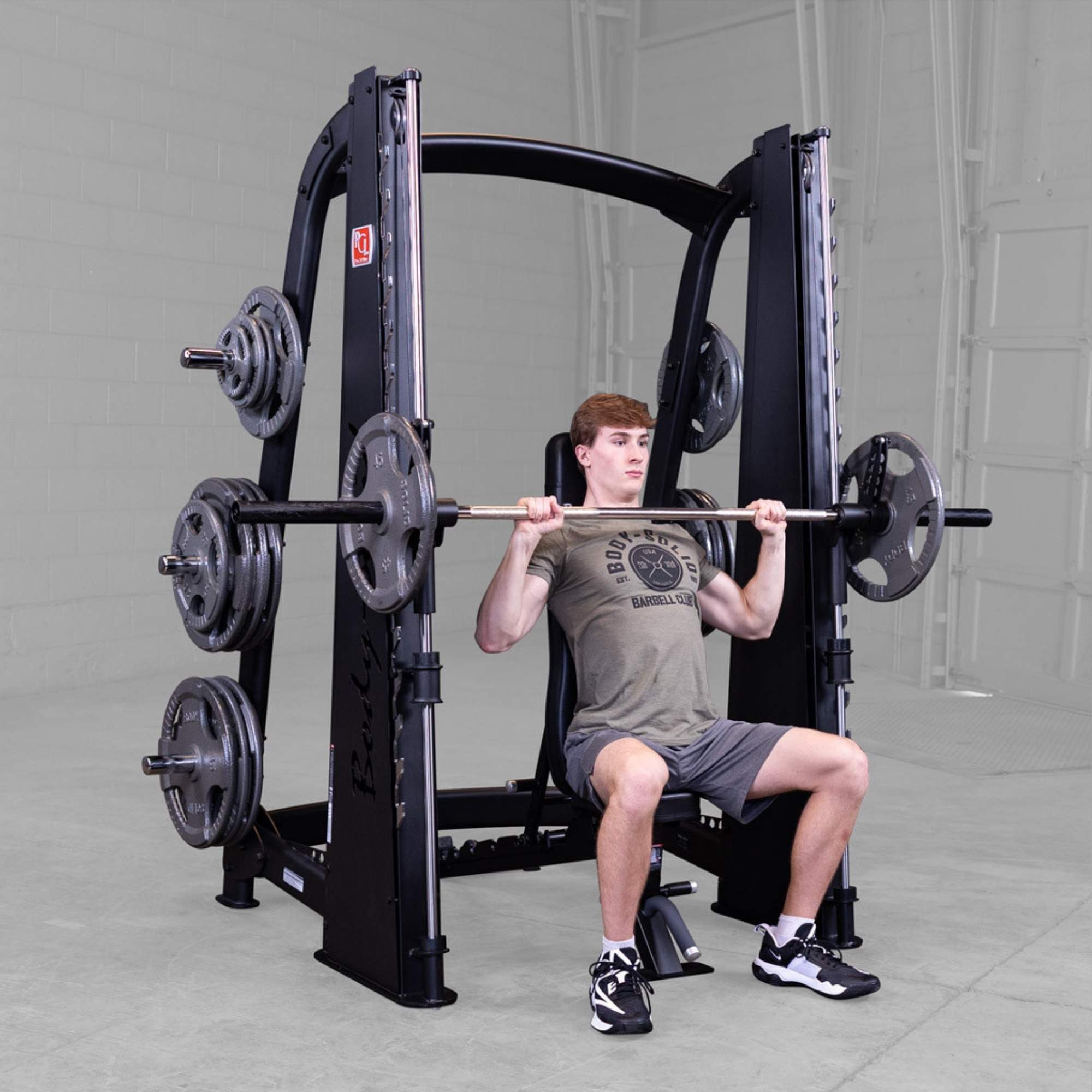 Body-Solid Proclub Counter Balanced Smith Machine SCB1000B A man performing a seated barbell shoulder press using a Smith machine with an adjustable bench in a gym.

