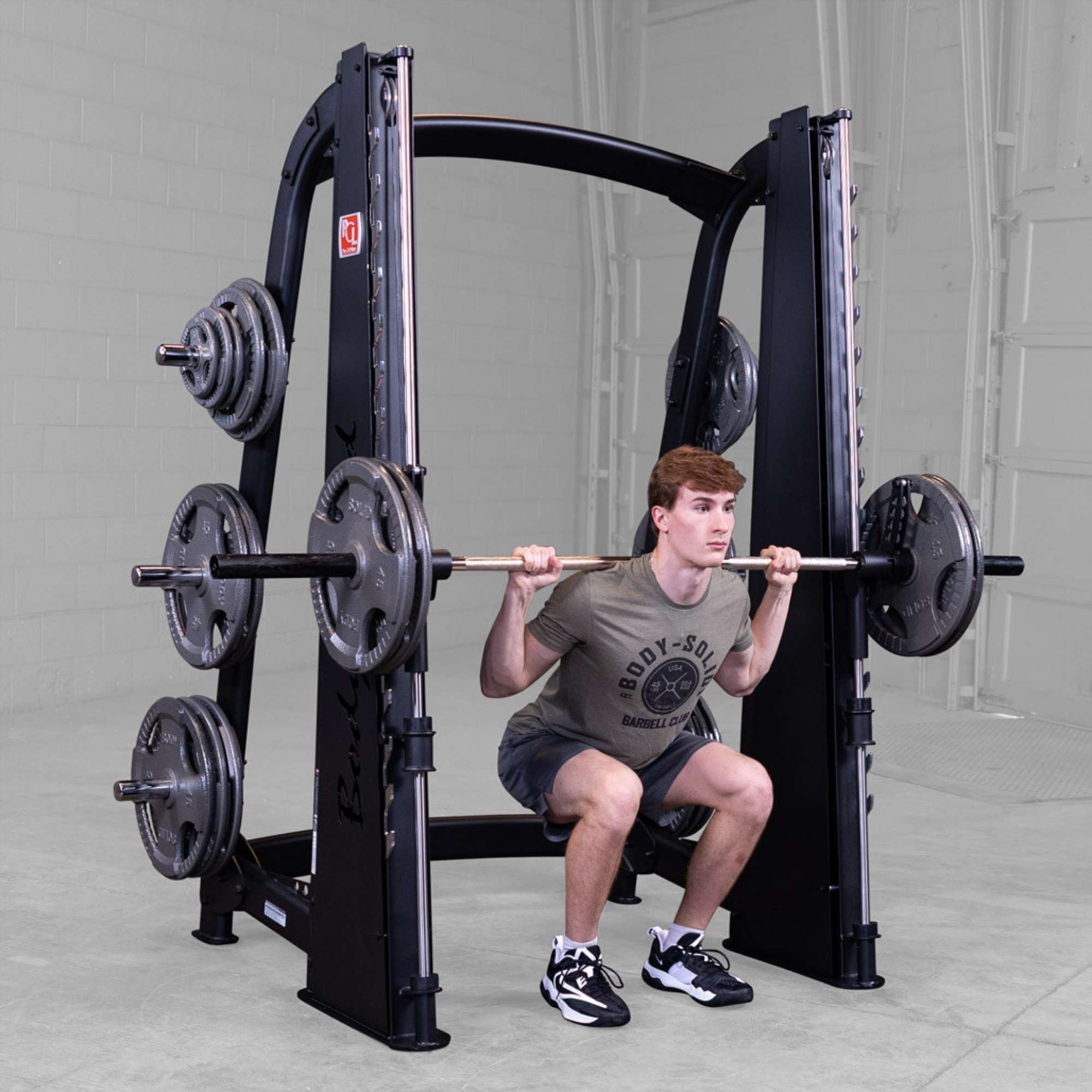 Body-Solid Proclub Counter Balanced Smith Machine SCB1000B Man performing a Smith machine squat with a loaded barbell in a gym.

