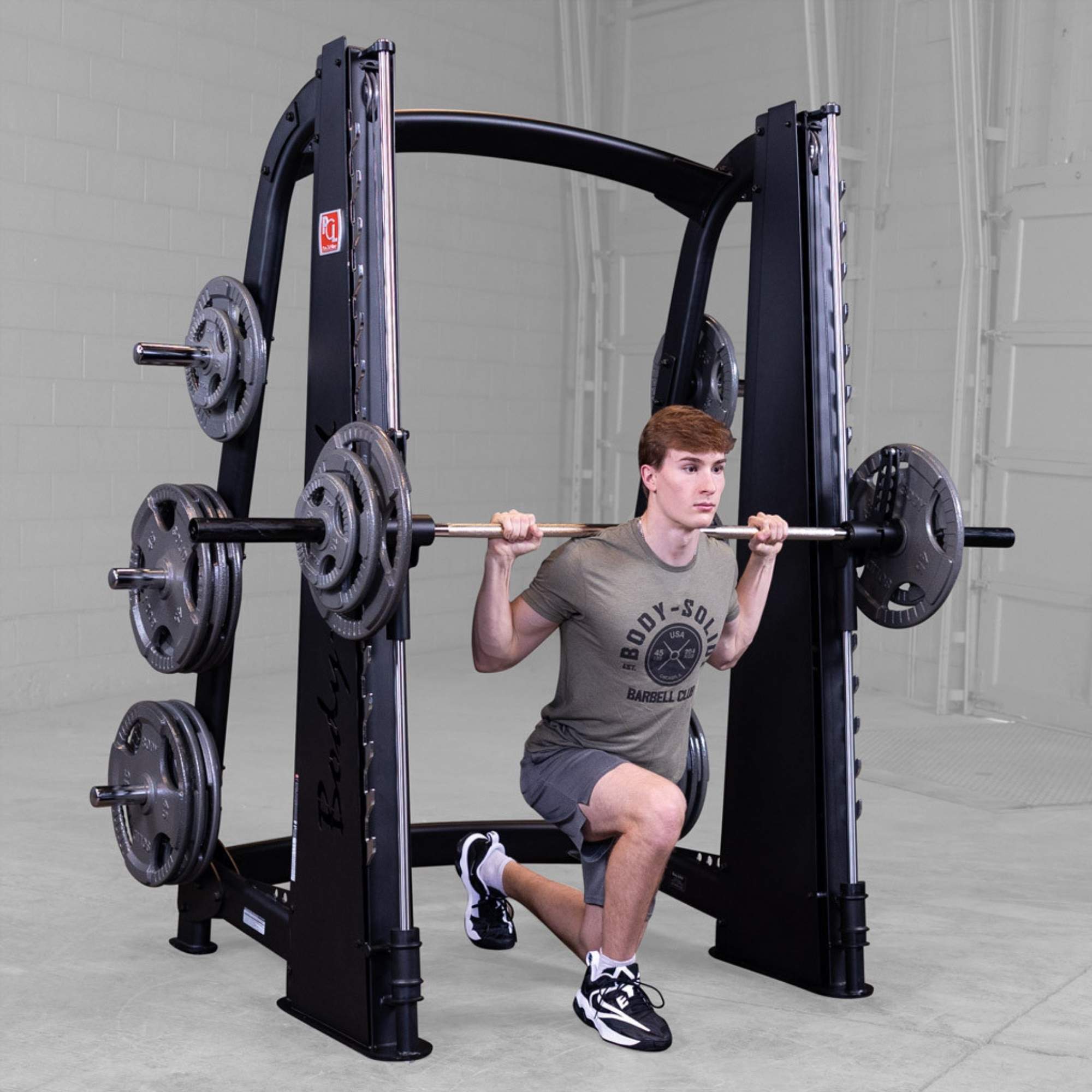 Body-Solid Proclub Counter Balanced Smith Machine SCB1000B Man performing a barbell reverse lunge on a Smith machine inside a gym.
