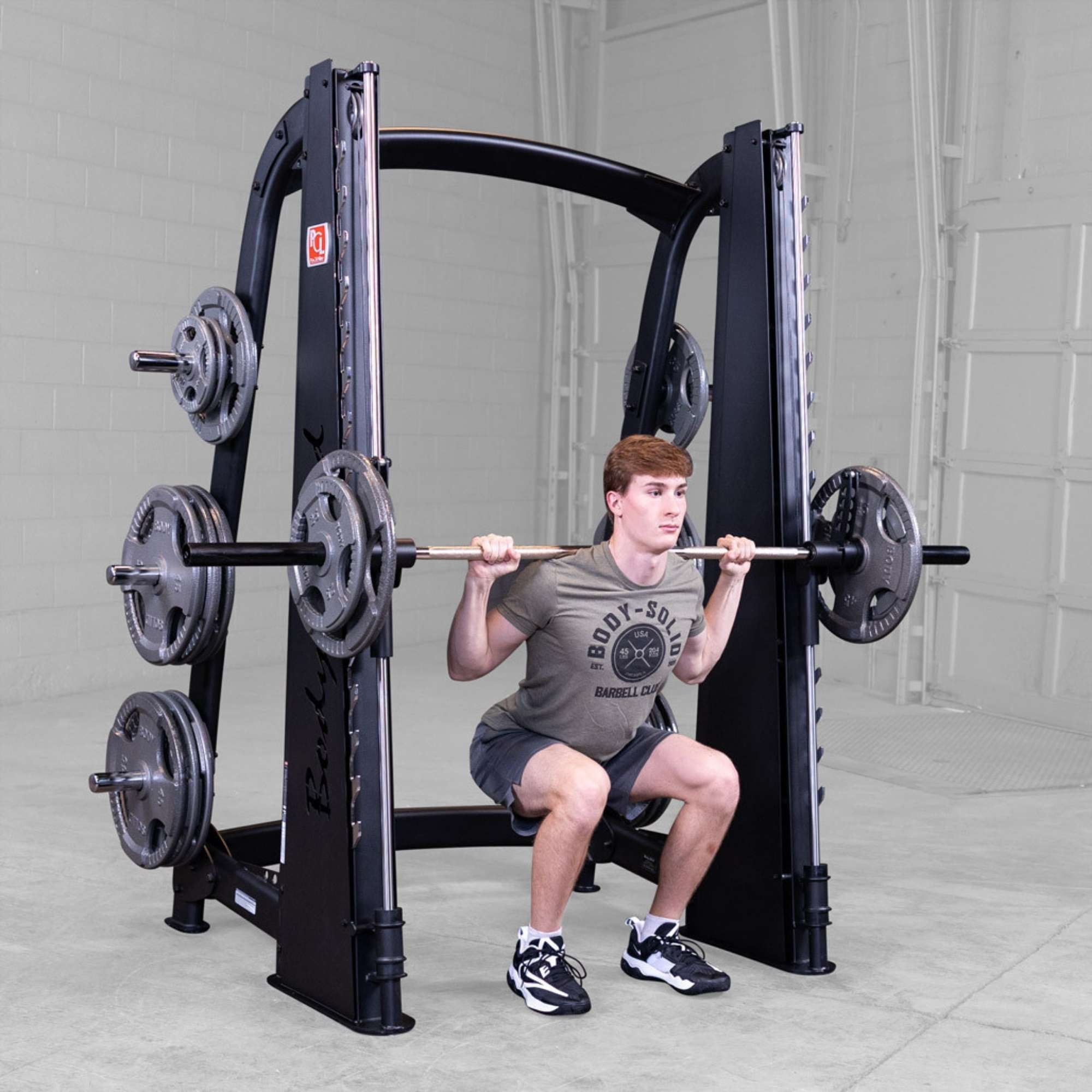 Body-Solid Proclub Counter Balanced Smith Machine SCB1000B Man squatting with a Smith machine barbell positioned on his shoulders in a gym environment