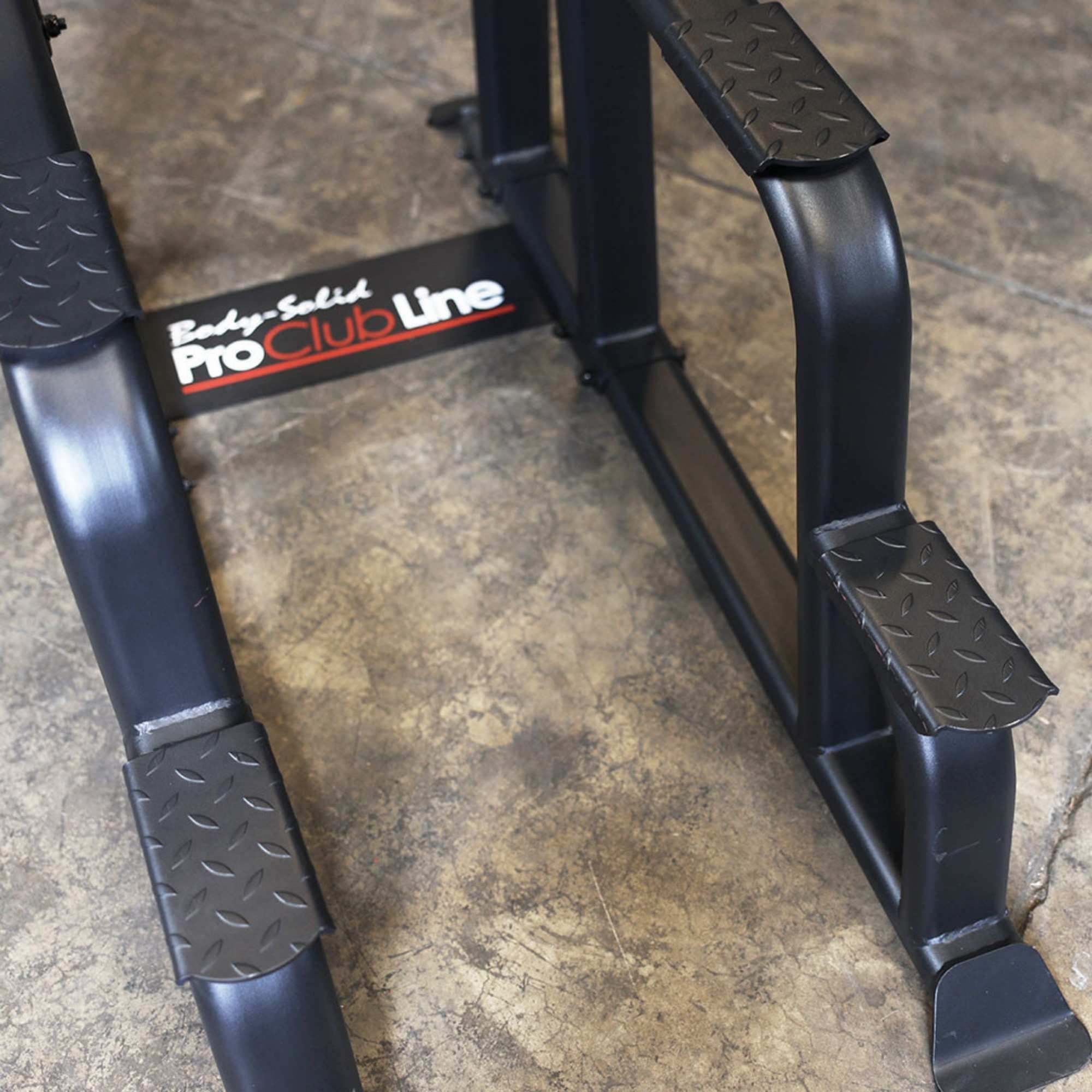Body-Solid Proclub Vertical Knee Raise SVKR1000BX Heavy-duty steel base of a Body-Solid Pro Club Line power tower with textured foot platforms on a concrete gym floor.