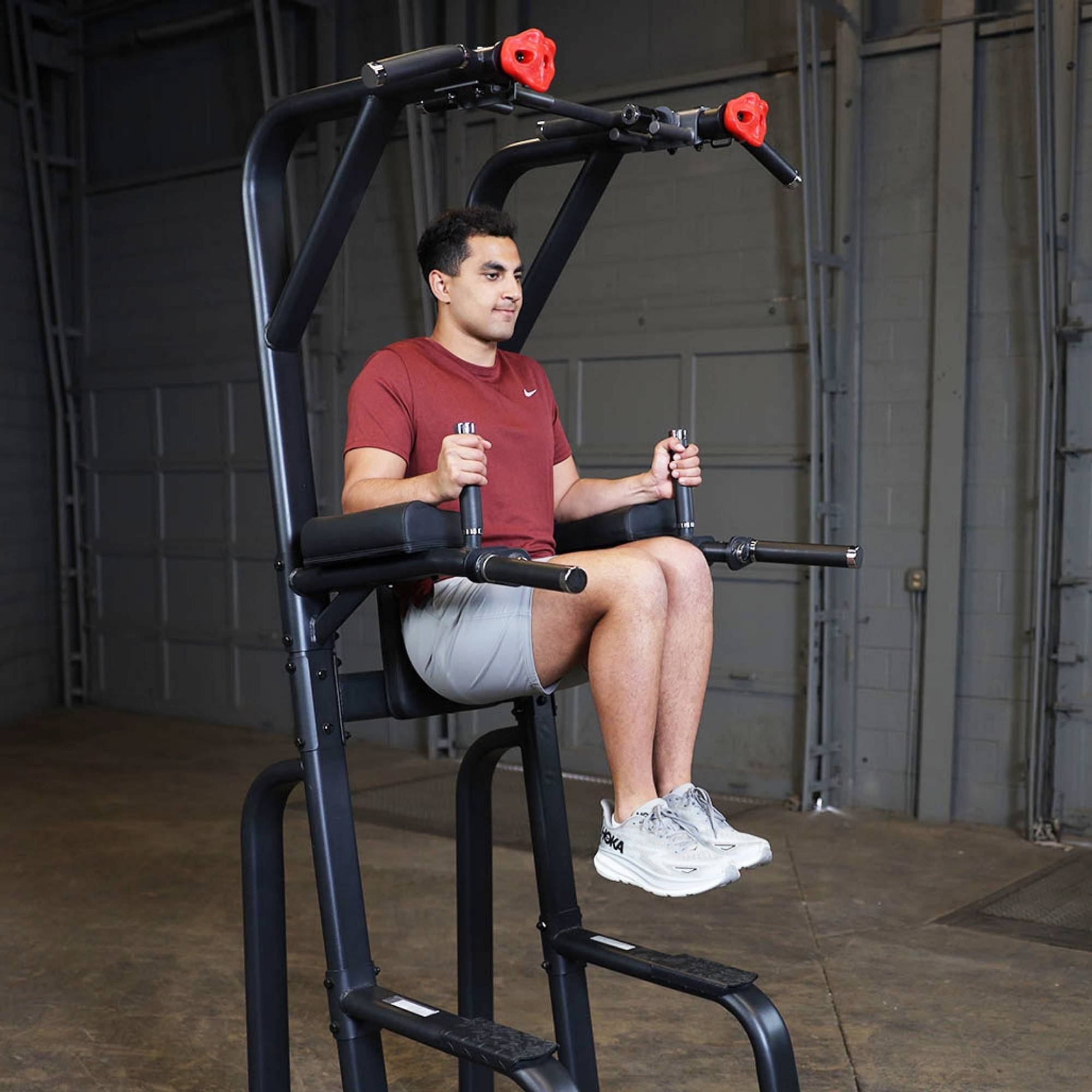 Body-Solid Proclub Vertical Knee Raise SVKR1000BX Man performing a knee raise exercise on a black power tower in an industrial-style gym.
