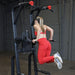 Body-Solid Proclub Vertical Knee Raise SVKR1000BX Woman in red activewear performing a dip exercise on a power tower dip station.