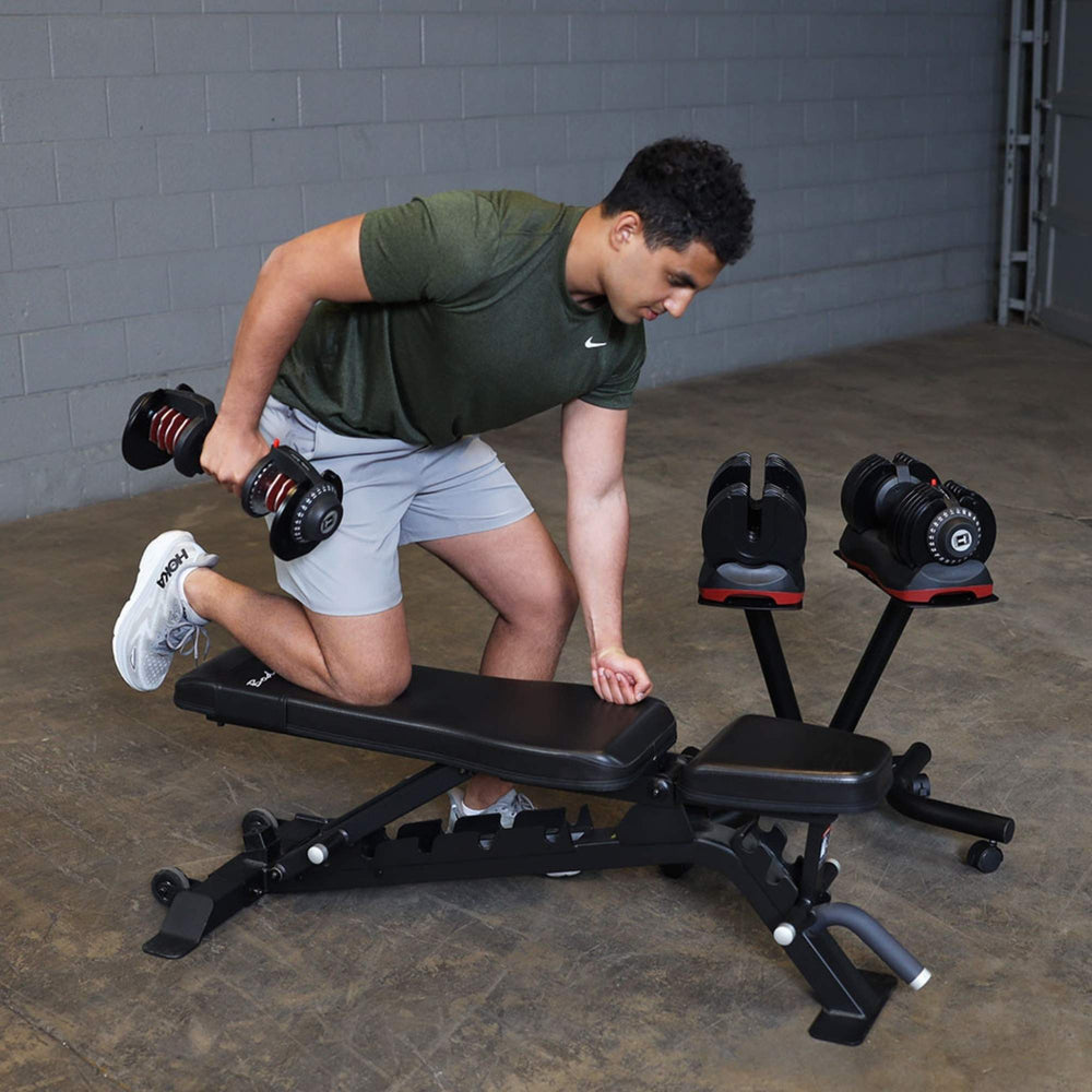Body-Solid Tools Adjustable Dumbbell Set, 11 lb. to 66 lb. with Stand SDBX132ST Man doing a single-arm dumbbell row on a workout bench next to a set of adjustable dumbbells