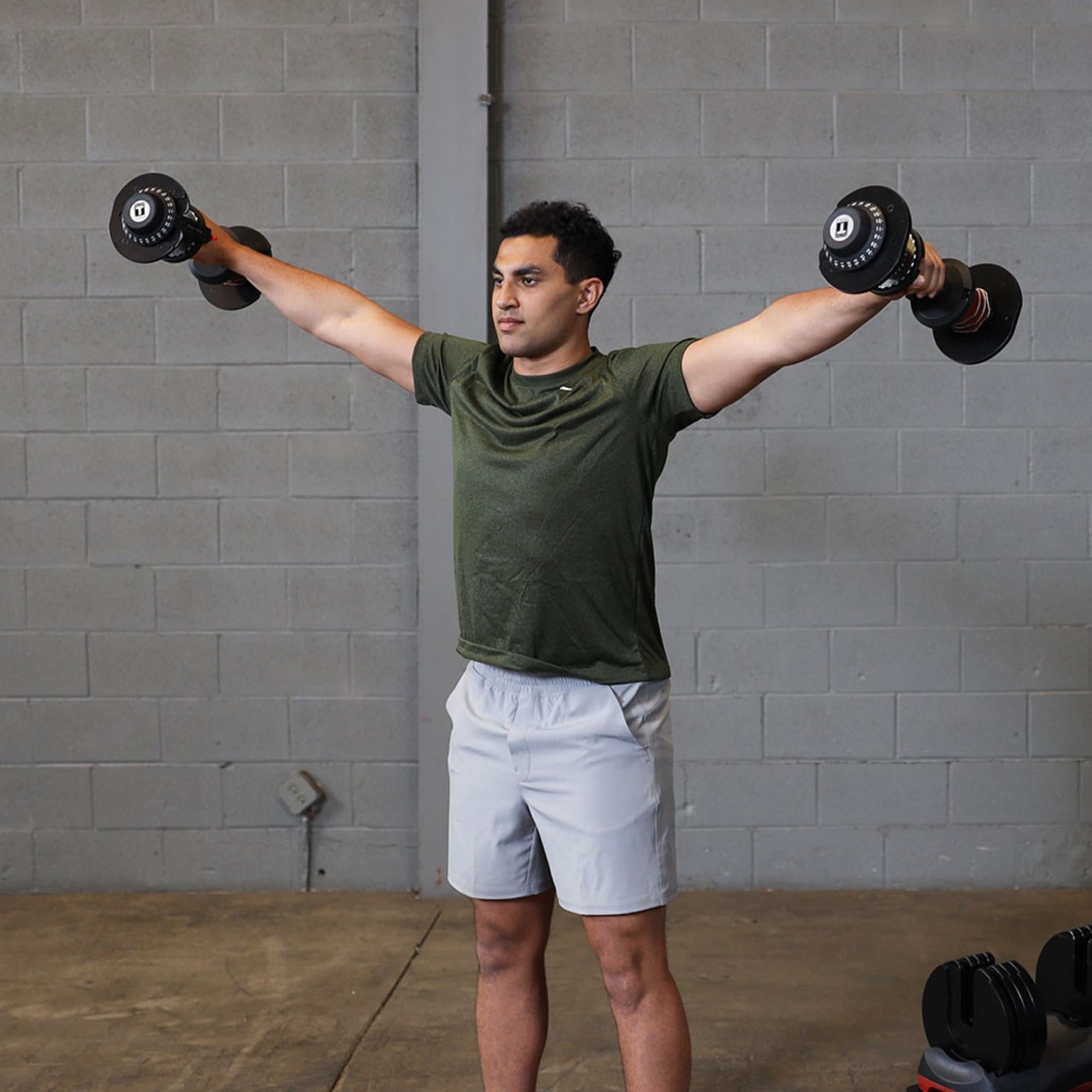 Body-Solid Tools Adjustable Dumbbell Set, 11 lb. to 66 lb. with Stand SDBX132ST Man executing a lateral raise exercise with adjustable dumbbells in a gym