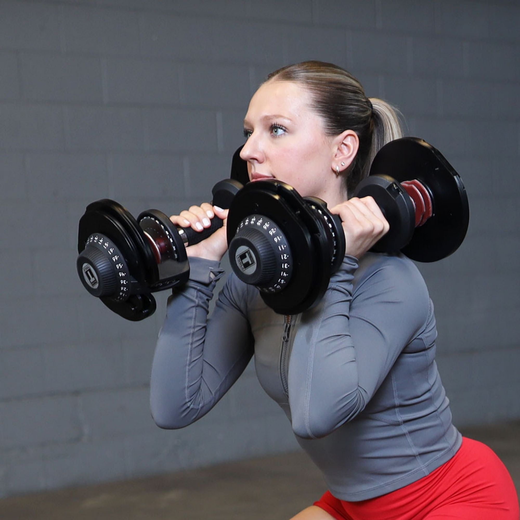 Body-Solid Tools Adjustable Dumbbell Set, 11 lb. to 66 lb. with Stand SDBX132ST Woman performing squat exercise holding adjustable dumbbells at shoulder height in a gym