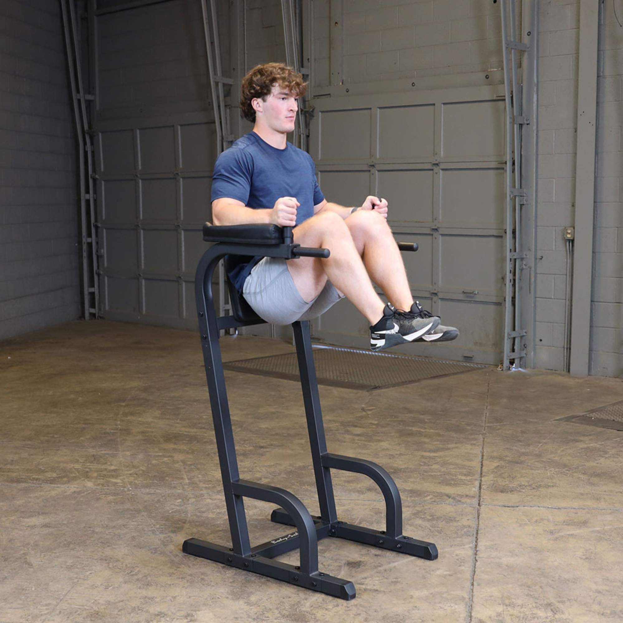 Body-Solid Vertical Knee Raise and Dip GVKR60B Man lifting knees while holding onto the Body-Solid vertical knee raise and dip station