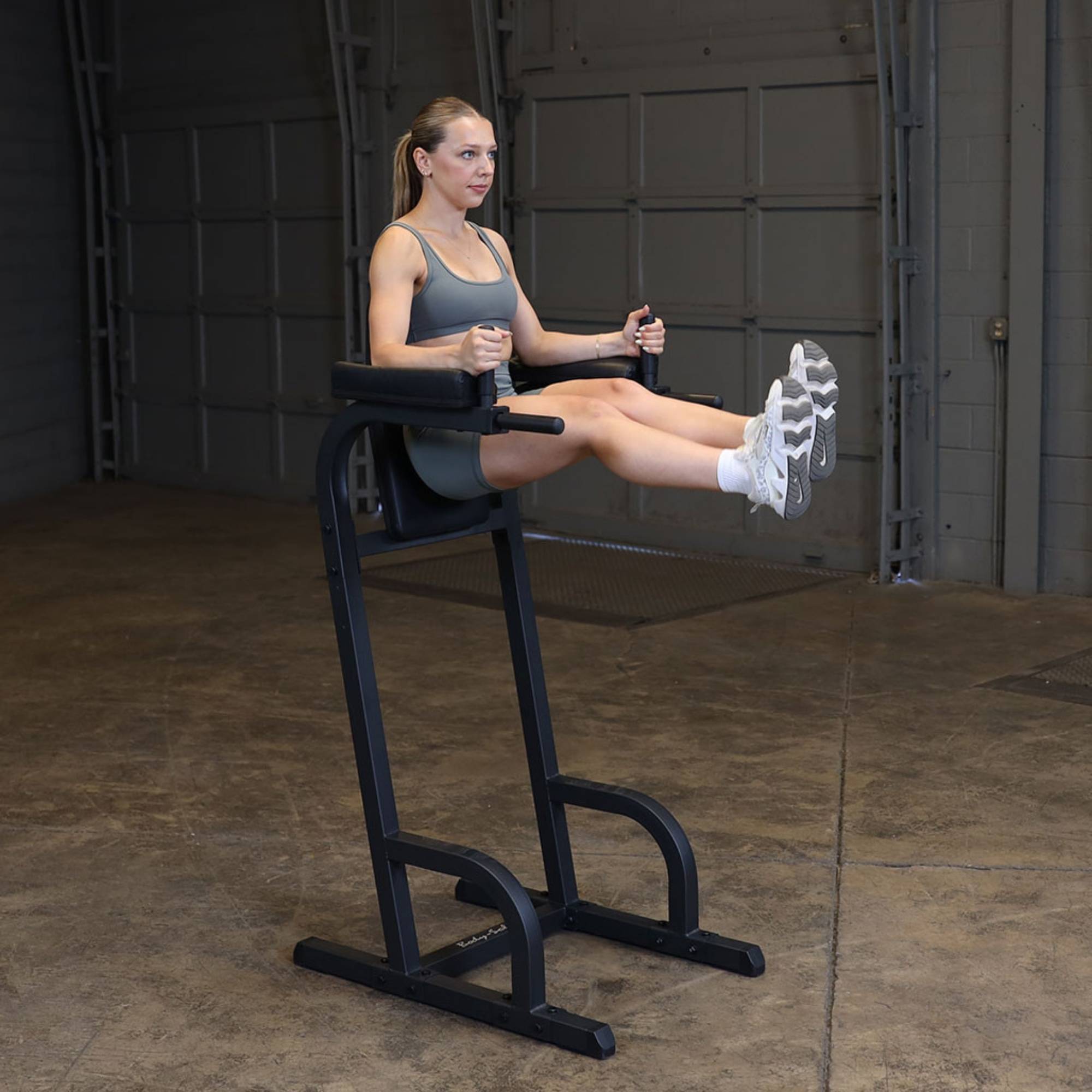 Body-Solid Vertical Knee Raise and Dip GVKR60B Woman lifting her legs straight out while using the Body-Solid VKR station for core training
