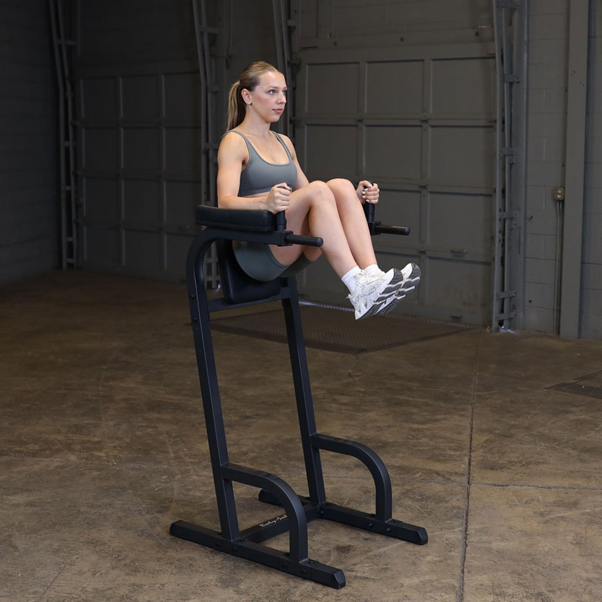 Body-Solid Vertical Knee Raise and Dip GVKR60B Woman performing knee raises on a Body-Solid vertical knee raise and dip station in a gym setting