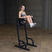 Body-Solid Vertical Knee Raise and Dip GVKR60B Woman performing knee raises on a Body-Solid vertical knee raise and dip station in a gym setting