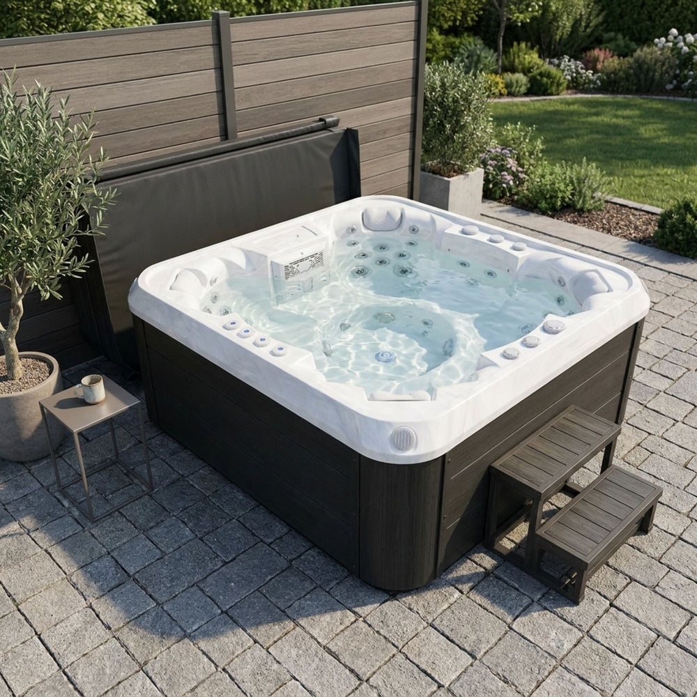 Luxury Spas USA Denali 7 person Hot tub on a paved patio with garden and wooden fence in the background