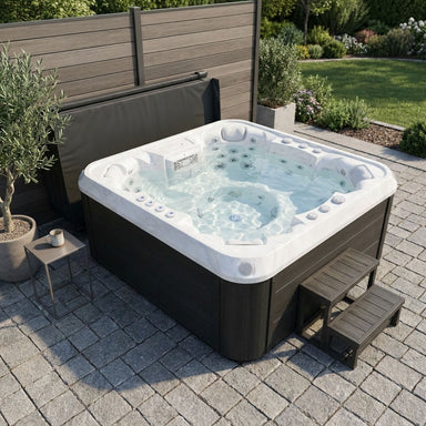 Luxury Spas USA Denali 7 person Hot tub on a paved patio with garden and wooden fence in the background