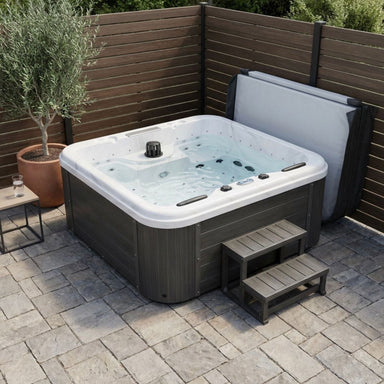 Luxury-Spas-Social-5-Person Hot tub with steps on a stone patio area with wooden walls and a plant.