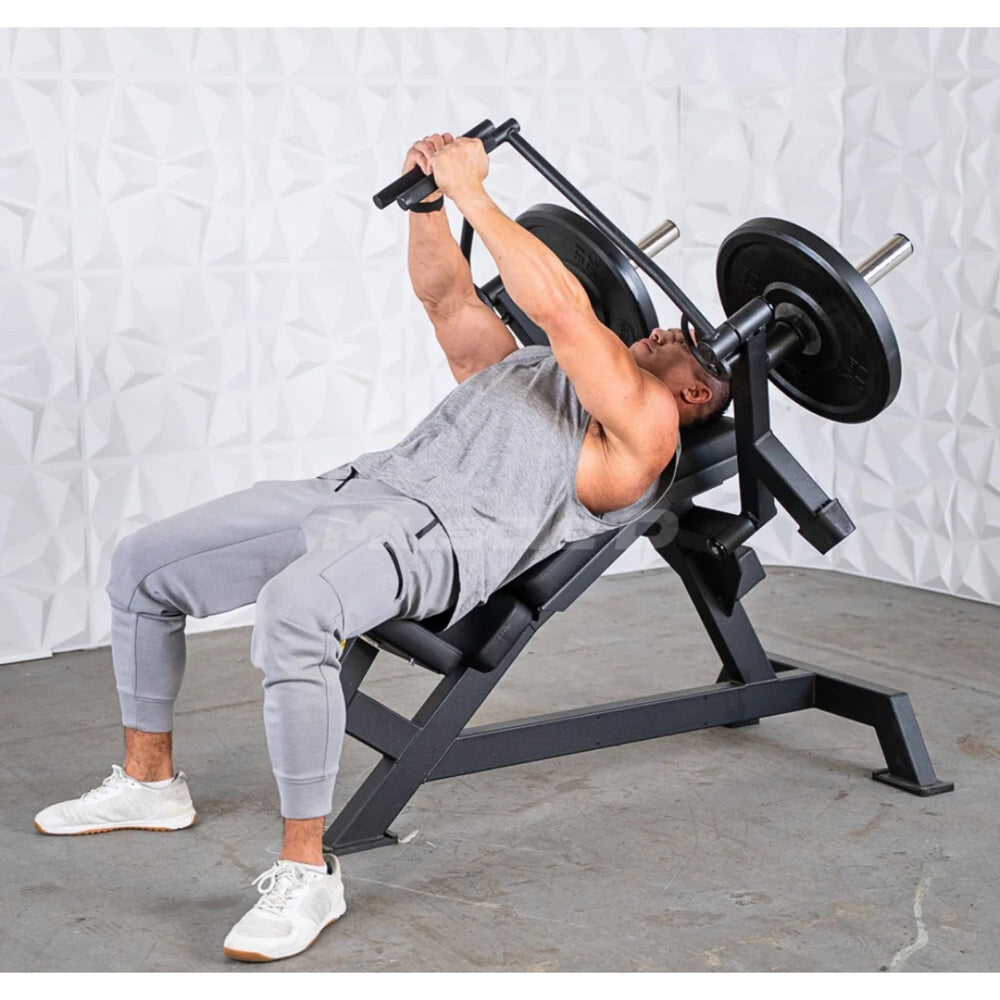 A man in a grey athletic outfit performing a  leverage pec fly bench bench press on a black adjustable weight bench with weight plates, set against a textured white wall and grey concrete floor.