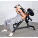 A man in a grey athletic outfit performing a  leverage pec fly bench bench press on a black adjustable weight bench with weight plates, set against a textured white wall and grey concrete floor.