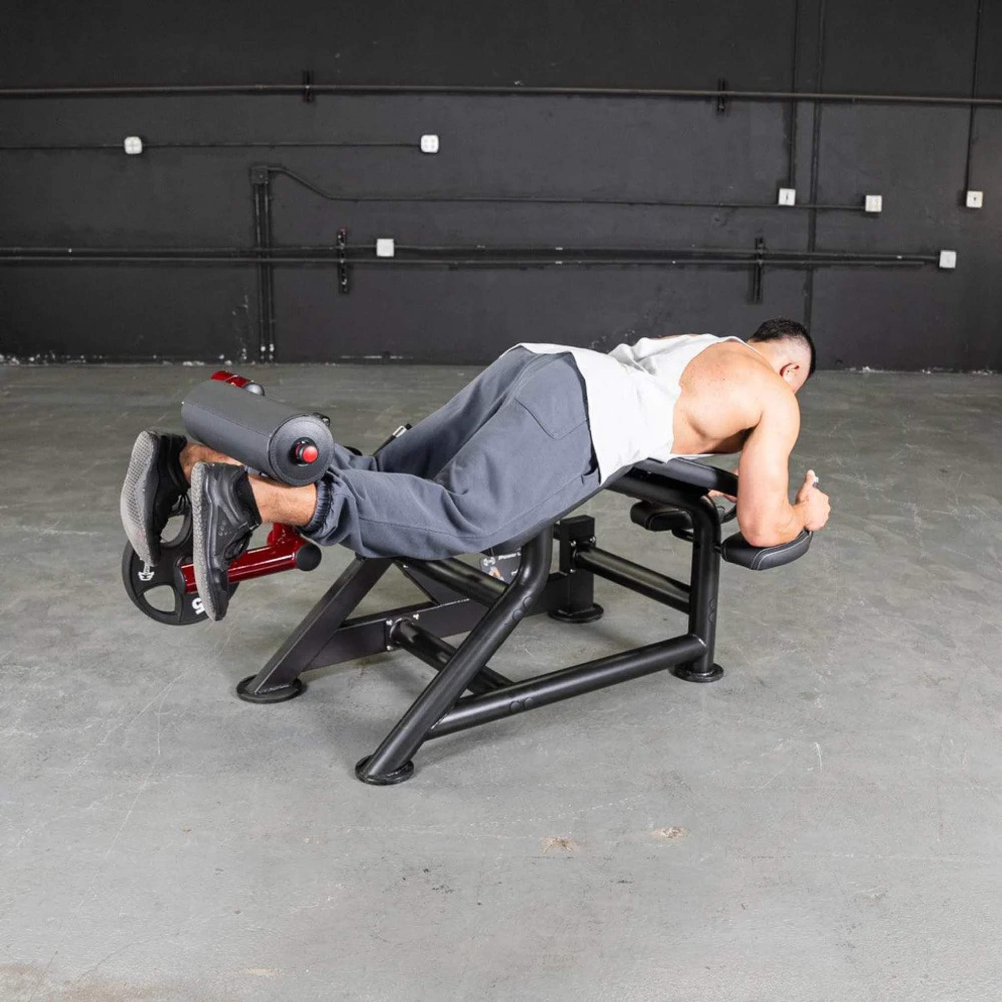 Athlete performing on the Muscle D Power Leverage V2 Prone Leg Curl machine with 25 lb Olympic plates for intense leg training.