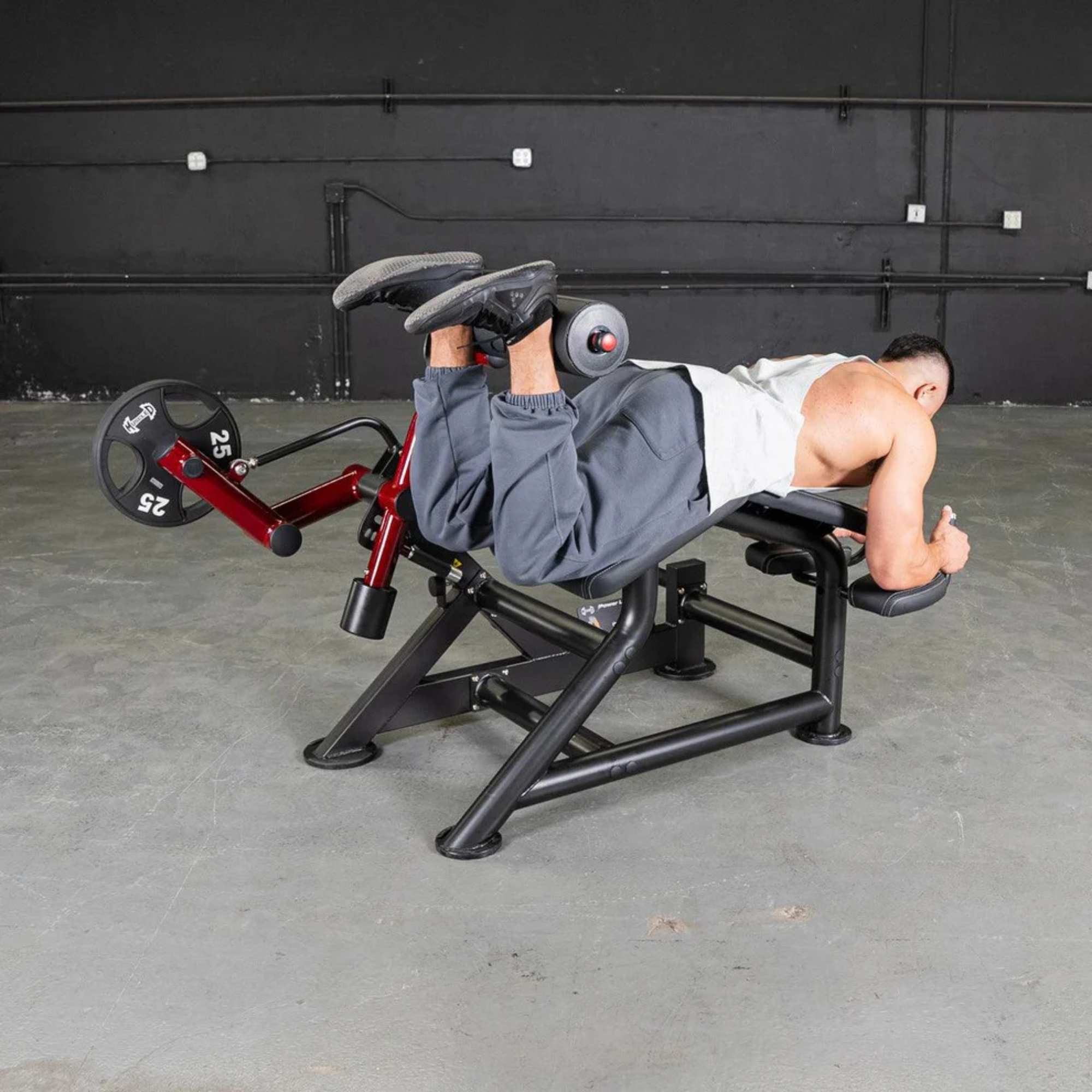 Bodybuilder demonstrating Muscle D Power Leverage V2 Prone Leg Curl with 45 lb Olympic plates, highlighting heavy-duty performance.