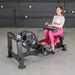 Female athlete seated on the Muscle D Power Leverage V2 Seated Calf Tib PL-PV2-SCT performing tibialis raises with 45-lb plates.