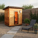SunRay Denali 4 Person Contemporary Outdoor Sauna  with Harvia 6kW Heater and Metal Roof 400D5 with a lounge chair and plants in a garden setting