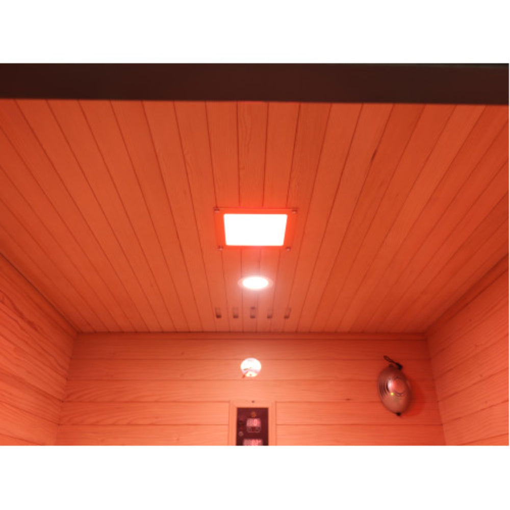 A square red light therapy panel mounted on the ceiling of a  Sunray Pacific 4-Person Outdoor Infrared Sauna , with warm orange ambient lighting illuminating the wood-paneled walls and ceiling.