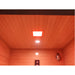 A square red light therapy panel mounted on the ceiling of a  Sunray Pacific 4-Person Outdoor Infrared Sauna , with warm orange ambient lighting illuminating the wood-paneled walls and ceiling.