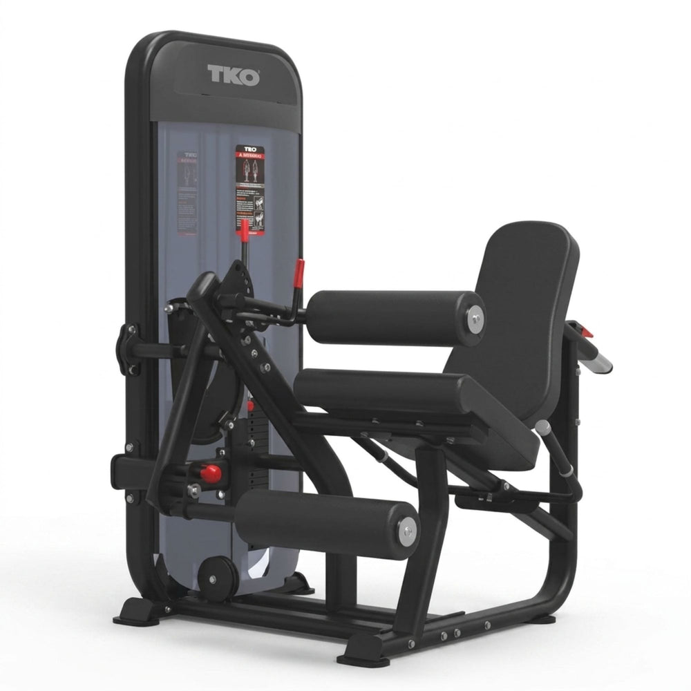 A TIO brand leg extension gym machine in black and gray, shown from a three-quarter angle on a solid white background.