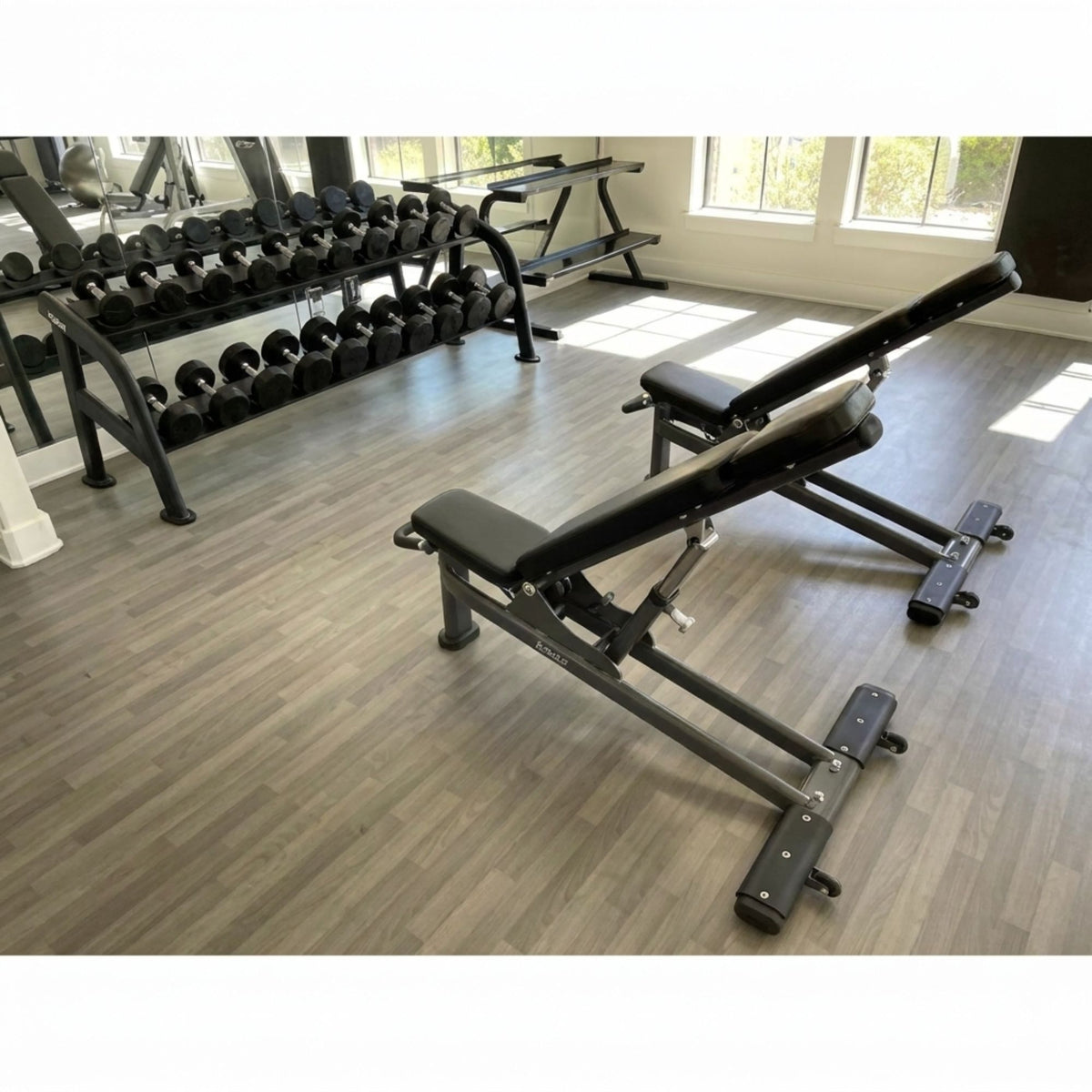 Black adjustable weight bench in a gym setting with weights and exercise equipment in the background.