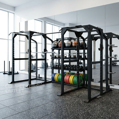 A black TKO Annex Dual Power Rack & Storage System 920PR-ANX multi-functional power rack in a modern gym setting, featuring a built-in storage shelf with kettlebells and colorful weight plates, with other gym equipment visible in the background.