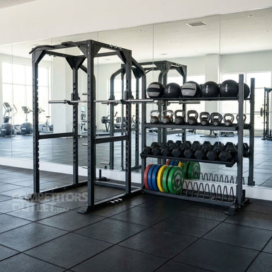 A black TKO Power Rack with Storage 920PR-STRG gym weight rack system with a pull-up cage, shelves holding black kettlebells and medicine balls, and a plate rack with colorful weight plates, set in a modern gym with mirrors and black rubber flooring.