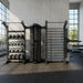 A black Torque-X-Create-Cable-Column-Stall-Bar-Training-Wall-with-Dip-Attachment-Plyo-step-front-facing-with-accessories system with a pull-up bar, horizontal bar, and weight rack shelves holding kettlebells, set in a modern gym with concrete walls and windows.