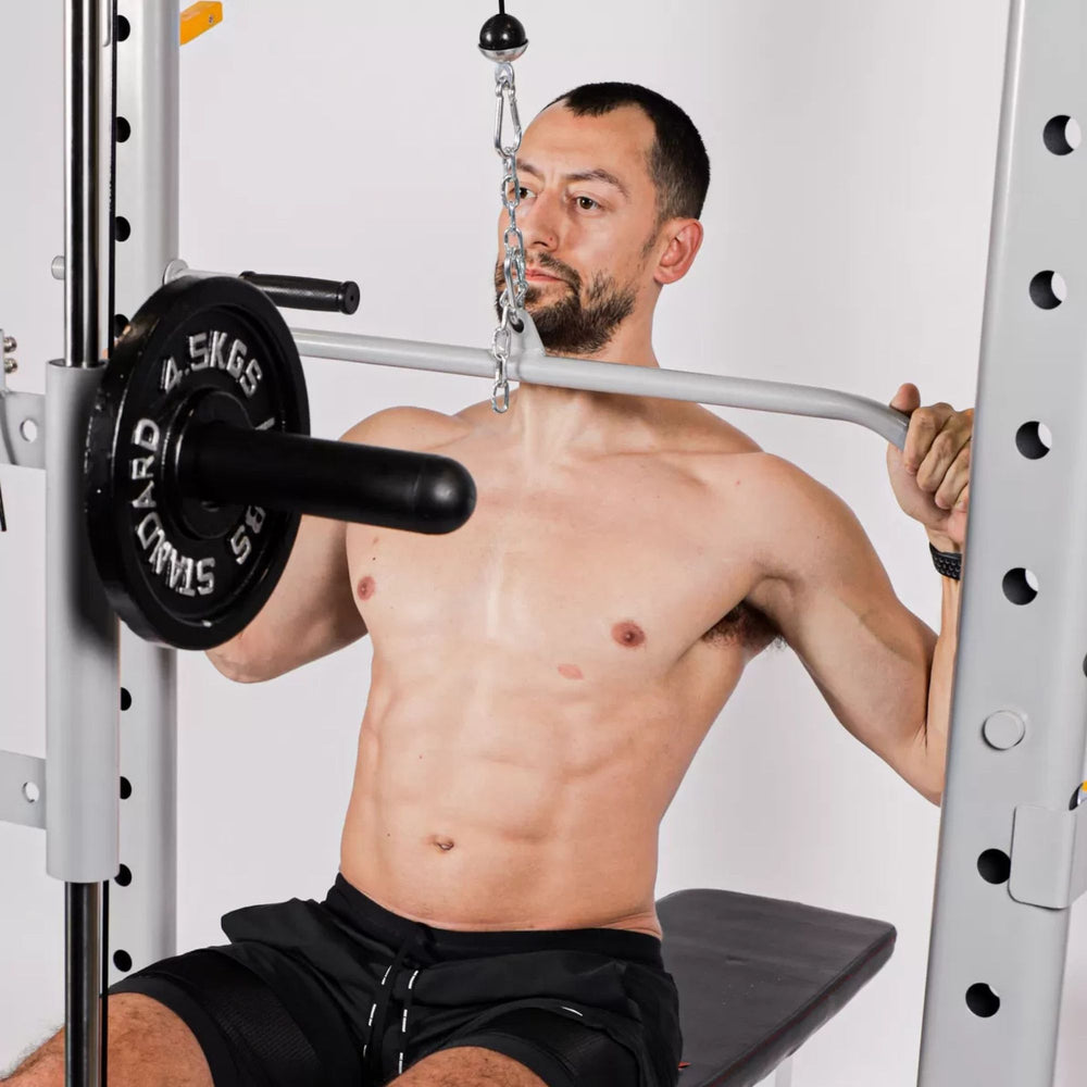 Vortex Squat Cage With High/low Pulley, Dip Attachments and Landmine SRVXG350 Shirtless man using lat pulldown bar on Smith machine with seated bench and weight plates